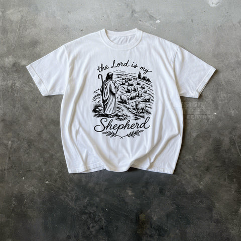 White t-shirt printed with black line art of a shepherd with a staff among sheep and the text the Lord is my Shepherd.