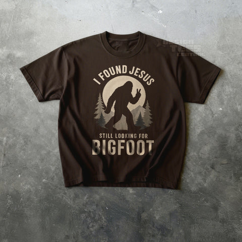 Brown t-shirt printed with a Bigfoot silhouette making a peace sign and the text I Found Jesus, Still Looking for Bigfoot.