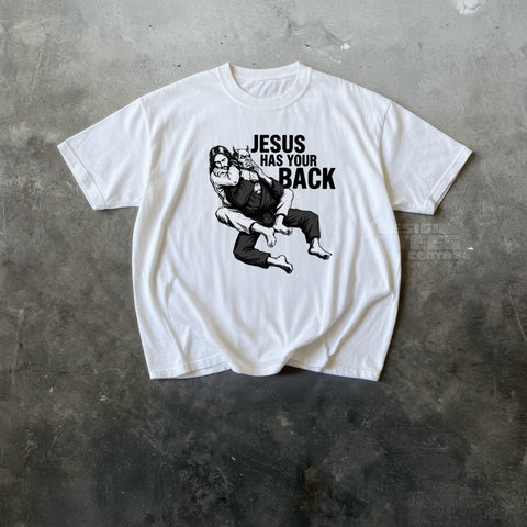 White t-shirt printed with an ink drawing of a bearded figure grappling a horned demon and the text Jesus Has Your Back.