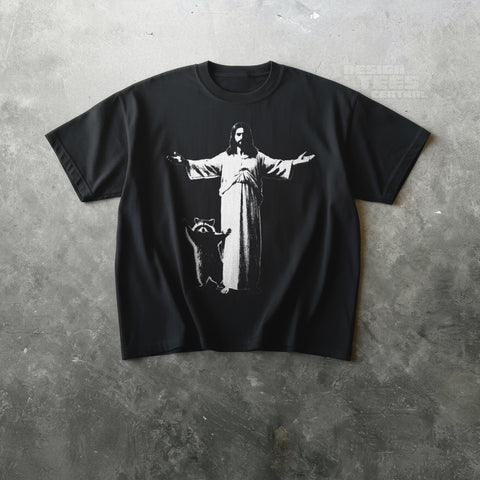 Black t-shirt printed in white with a robed figure, arms outstretched, beside a raccoon standing on its hind legs.